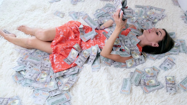 很多钱和一个漂亮的女孩睡在一张白色的床上。巨大财富的概念视频下载