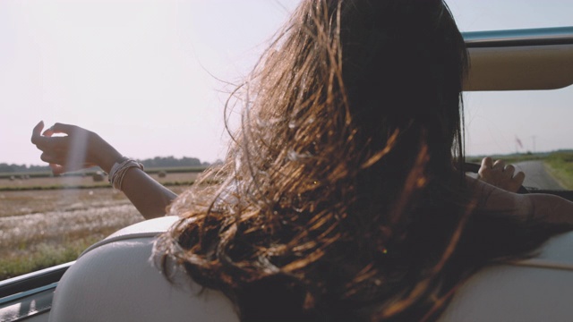风吹着无忧无虑的年轻女子的头发，开着敞篷车沿着阳光明媚的乡村田野行驶视频下载