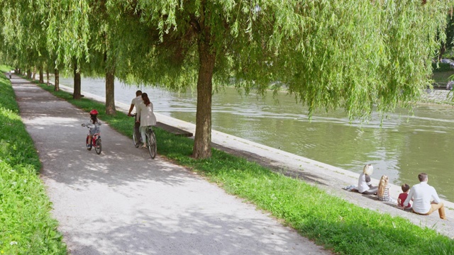 SLO MO CS小女孩骑着她的自行车沿着她的父母骑着双人自行车穿过公园视频下载