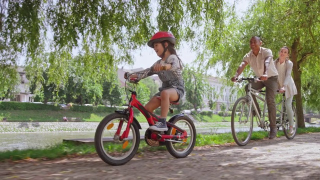一对夫妇骑着双人自行车，他们的小女儿在他们旁边穿过公园视频素材