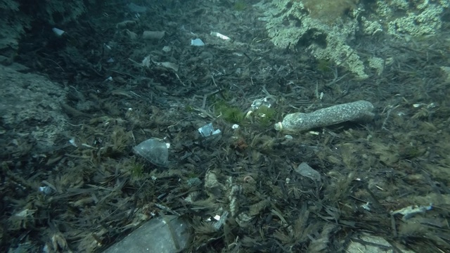 塑料污染，鱼群游过覆盖着大量塑料垃圾的海底。慢镜头，欧洲地中海海床上的塑料瓶、塑料袋和盘子。视频素材