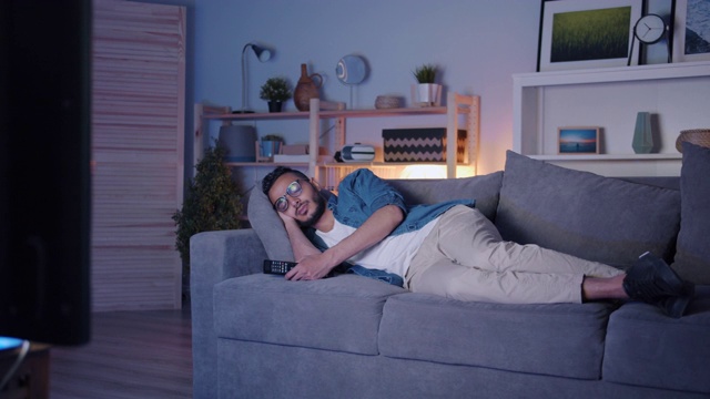 一个阿拉伯人，晚上睡在电视机前的沙发上，在黑暗的公寓里放松视频素材