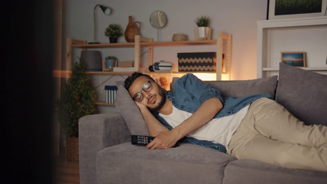 疲惫的中东男人独自躺在电视机前的沙发上视频素材