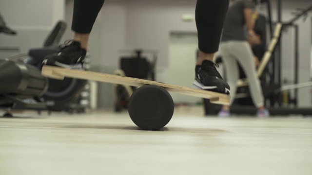 男子在健身房做运动的腿部特写。男子在用滚轴和滑板做平衡运动。视频下载
