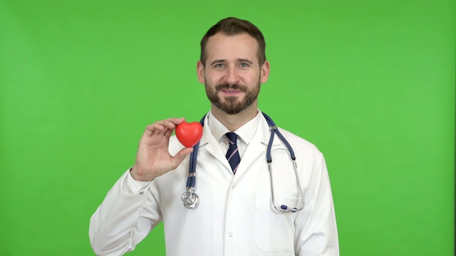 年轻男医生拿着一个心形，对着色度键微笑视频素材