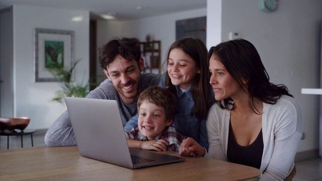 快乐的家庭在笔记本电脑上看视频，而孩子们指着屏幕，微笑着交谈视频素材