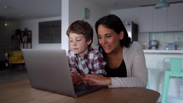 妈妈和儿子在笔记本电脑上寻找东西，而妈妈解释并指着屏幕视频素材