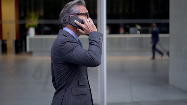 严肃的中年男企业家穿着昂贵的西装在漫游电话交谈的慢动作效果视频素材
