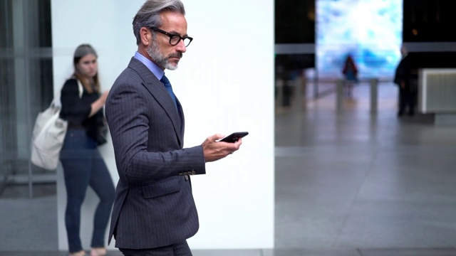 成功男士身着正装前往市中心服务中心，通过智能手机应用接收国际手机电话的慢动作效果视频素材