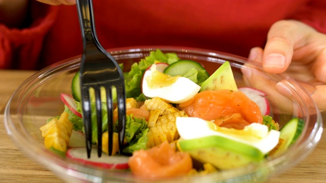 快餐店的顾客用叉子把蔬菜、鱼和鸡蛋插进沙拉里视频下载