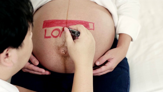 幸福时光:男人在他怀孕的肚子上写字视频素材