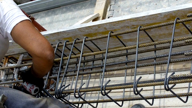 肮脏的工人用钳子和铁丝绑钢筋。视频下载