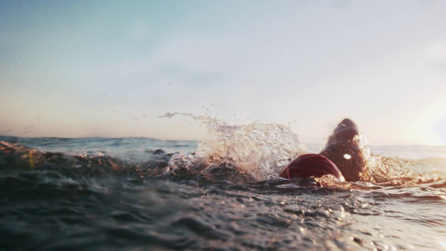 日落时，一个年轻人在海里游泳视频素材