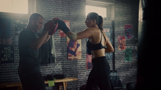 Fit Athletic Woman Kickboxer Punches and Hits the Punching Pads During a Workout in a Loft Gym.她是美丽和精力充沛的。强壮教练拿着拳击垫。强烈的自卫训练。视频下载
