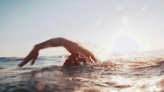 日落时，一个年轻人在海里游泳视频素材