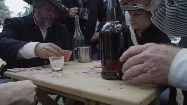 一个棕色的大瓶子放在桌子上，人们打扮成内战士兵在打牌。视频下载