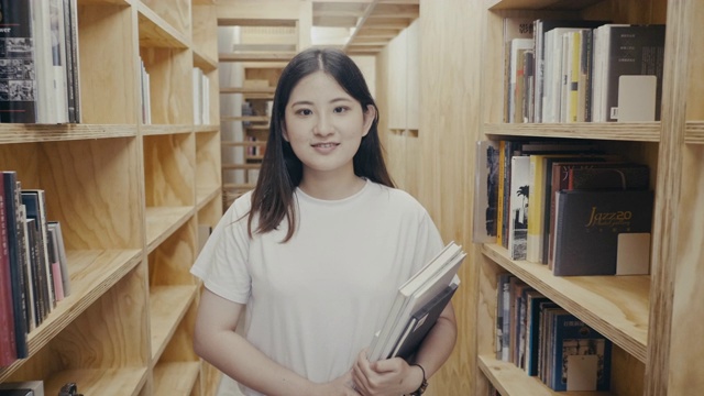 一个可爱的年轻亚洲女学生走在书架之间的肖像(慢镜头)视频素材