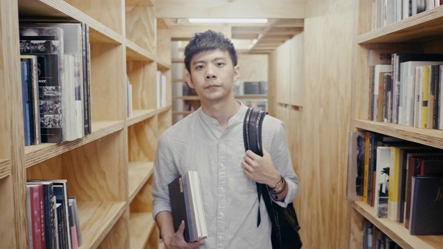 一个年轻的亚洲男学生在书架之间行走的肖像(慢镜头)视频素材