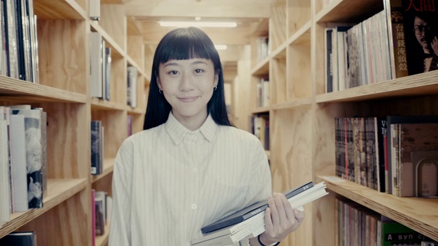 一个可爱的年轻亚洲女学生走在书架之间的肖像(慢镜头)视频素材