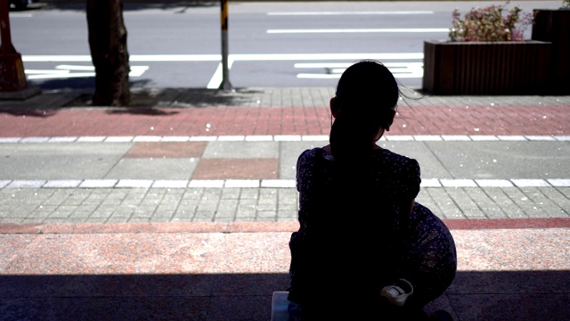 一个小女孩坐在公共汽车站的剪影。视频素材