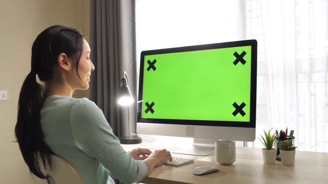 亚洲女人用绿色屏幕在家里的电脑，多莉拍摄视频素材