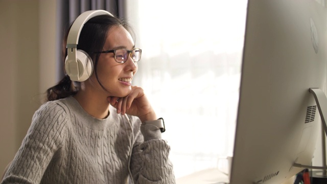 亚洲妇女在家使用电脑时戴耳机视频素材