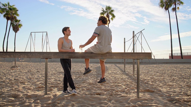 两个年轻的朋友，拉丁裔和白种人，坐在和休息在肌肉海滩户外运动区健身锻炼后。威尼斯海滩，圣塔莫尼卡，洛杉矶，加州，美国。视频素材