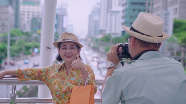 一位老人在阳台上与粉丝们合影，以泰国首都为背景。视频下载