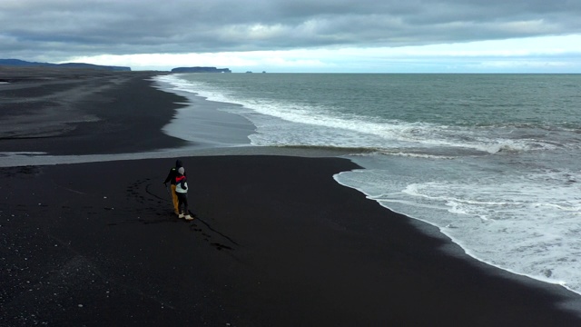 航拍一对夫妇站在冰岛的黑沙滩上视频素材