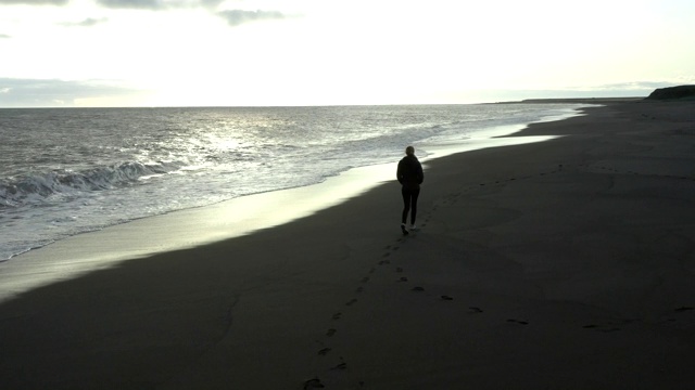 一名年轻女子走在冰岛的黑沙滩上视频素材