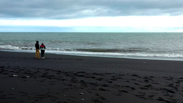 航拍一对夫妇站在冰岛的黑沙滩上视频素材