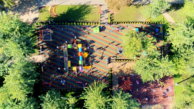 鸟瞰图城市公园大现代儿童游乐场之间的树与许多不同的滑梯，秋千和娱乐游乐设备充满了快乐的孩子与父母享受玩耍。视频下载