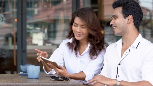 4K媒体拍摄的聪明的亚洲商人和女商人谈论和分享商业想法使用数字平板电脑和无线技术在咖啡店。户外办公理念。视频素材