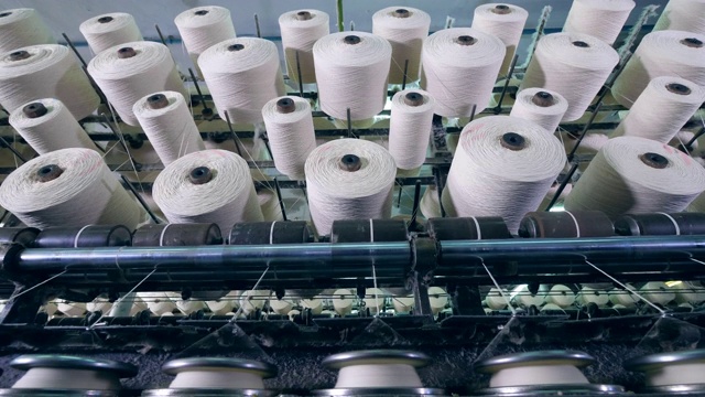 在工厂的机器上纺丝的许多线轴。纺织厂设备在工作。视频下载