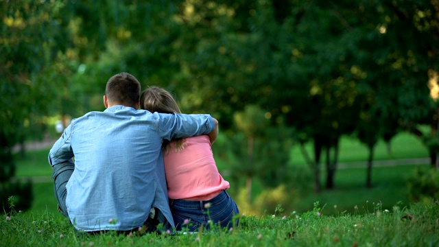 后视图的年轻夫妇拥抱和坐在草地上的公园，在一起视频下载