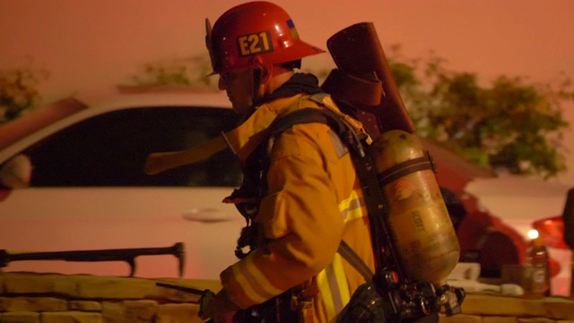 一名消防队员带着氧气罐在夜间扑灭居民区的一场房屋火灾。视频下载