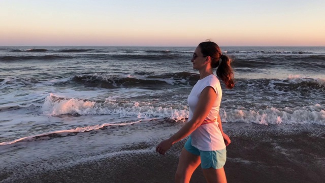 日落时分，一名女子在海滩上散步视频素材