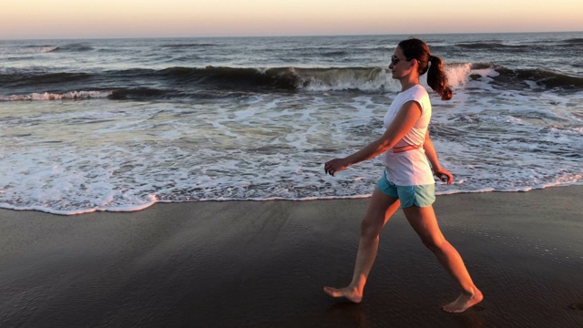 日落时分，一名女子在海滩上散步视频素材