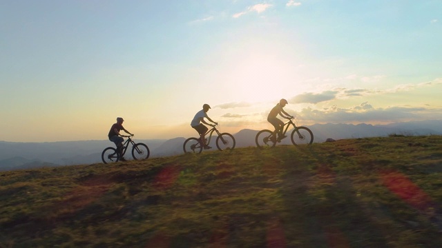 空中剪影:阳光明媚的日子里，适合的游客沿着长满草的小路骑自行车视频素材