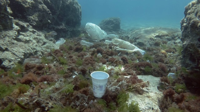 塑料污染，白色的塑料杯慢慢下沉，底部覆盖着大量的塑料碎片。缓慢的运动。欧洲地中海海床上的塑料瓶、塑料袋和盘子。视频素材