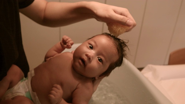 亚洲婴儿抱着爸爸的胳膊。在家洗头，温暖的光线，白天视频下载