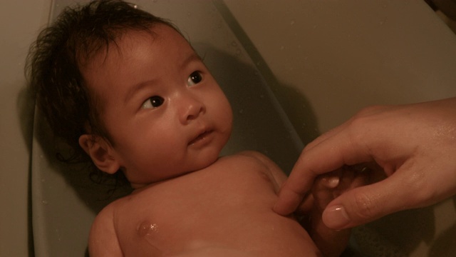 特写亚洲婴儿躺在浴缸里用她父亲的手和海绵洗澡，在家里视频素材