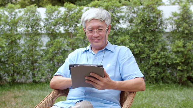 亚洲老年男性在家里使用平板电脑。亚洲资深华人男性在网上搜索关于如何健康的信息，而躺在家里的花园上午的概念。视频素材
