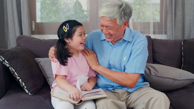 亚洲爷爷在家休息。高三语文，爷爷开心的和小孙女女儿一起享受在客厅看书和做作业的概念。慢动作镜头。视频下载