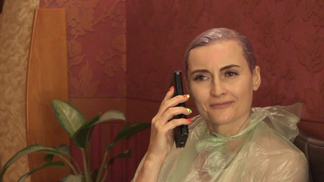 漂亮的年轻女子坐在染发的发型师坐在大厅里，正在打手机视频素材