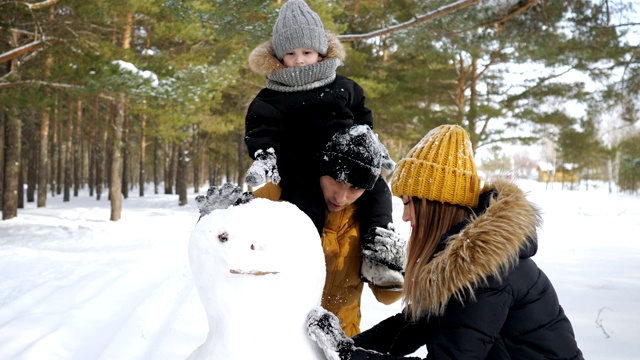 年轻的家庭，妈妈，儿子和爸爸在冬季城市公园堆雪人。视频素材