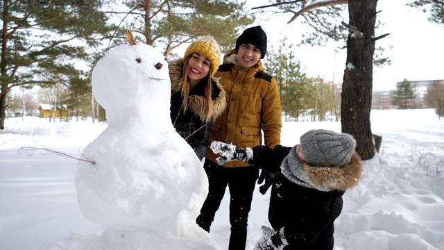 快乐的家庭妈妈，爸爸和儿子在冬季城市公园堆雪人。视频素材