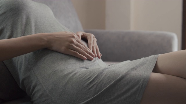 亚洲妇女有盆腔疼痛胃痛而坐在家里的沙发上视频素材