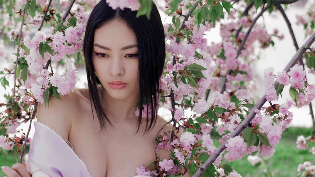 一个美丽的亚洲女孩的肖像户外对着春花树。后台视频下载