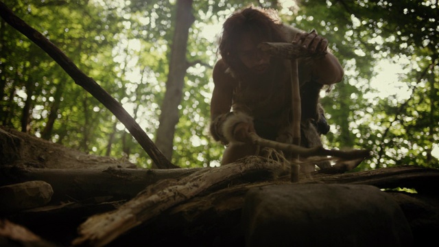 穿兽皮的原始穴居人用弓钻法生火的剪影。尼安德特人点燃人类文明史上第一次人造火。低角度拍摄视频素材